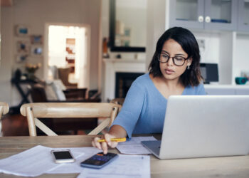 Shot of a young woman using a laptop and calculator while working from home